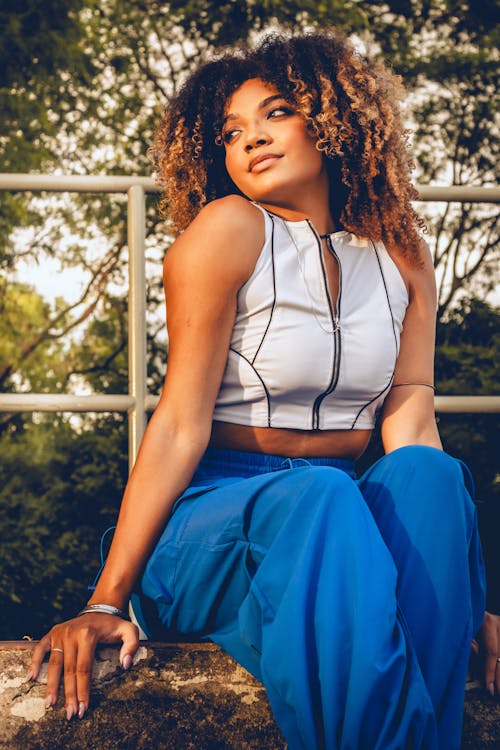 A woman with curly hair and blue pants sitting on a ledge