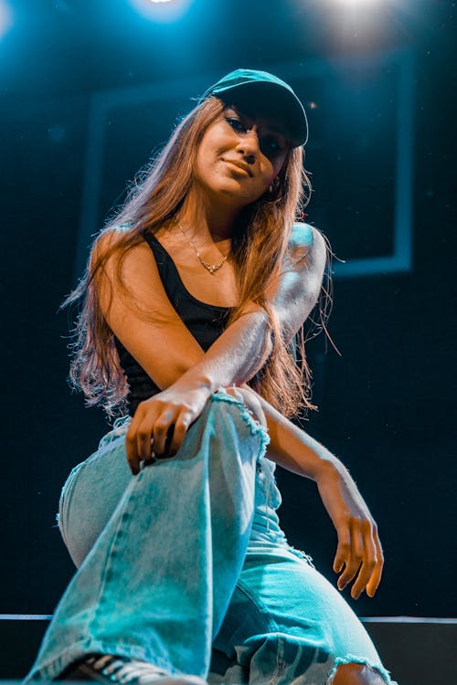A woman in jeans and a hat sitting on a stage