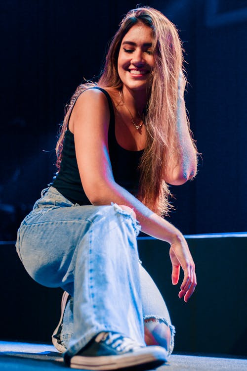 A woman in jeans and a top squatting on the stage