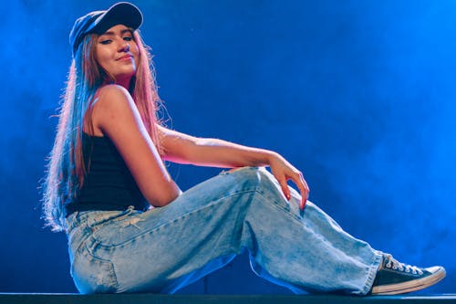 A girl in jeans and a cap sitting on a stage