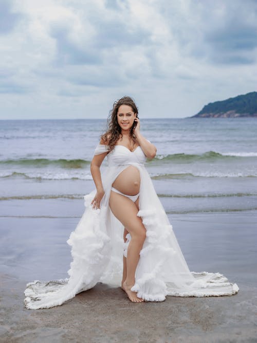 A pregnant woman in a white dress on the beach