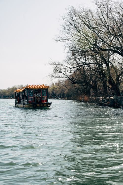 Free A traditional Chinese boat cruises on a calm lake in Beijing, surrounded by trees. Stock Photo