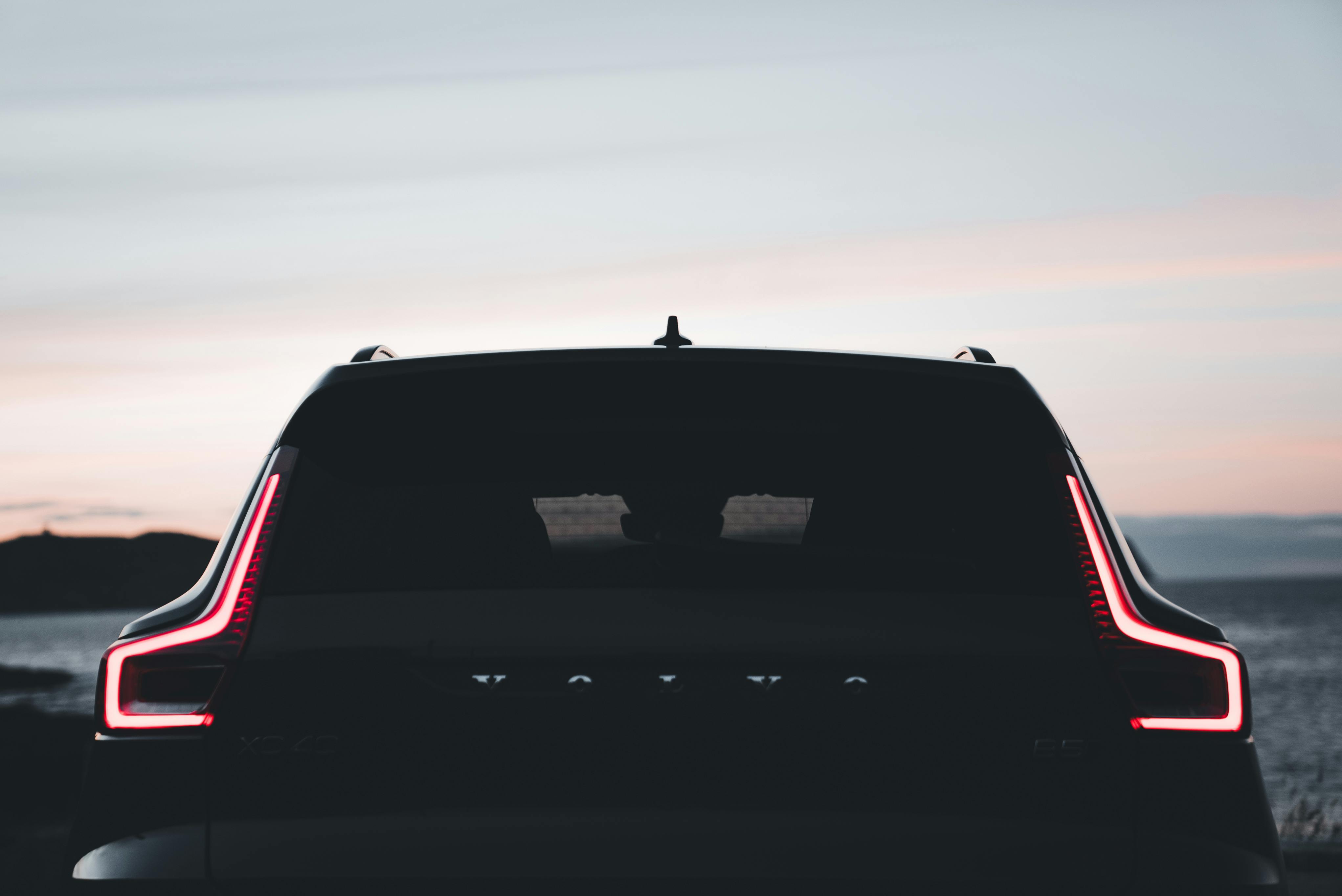 Silhouette of a Volvo SUV with illuminated tail lights at a coastal twilight setting.