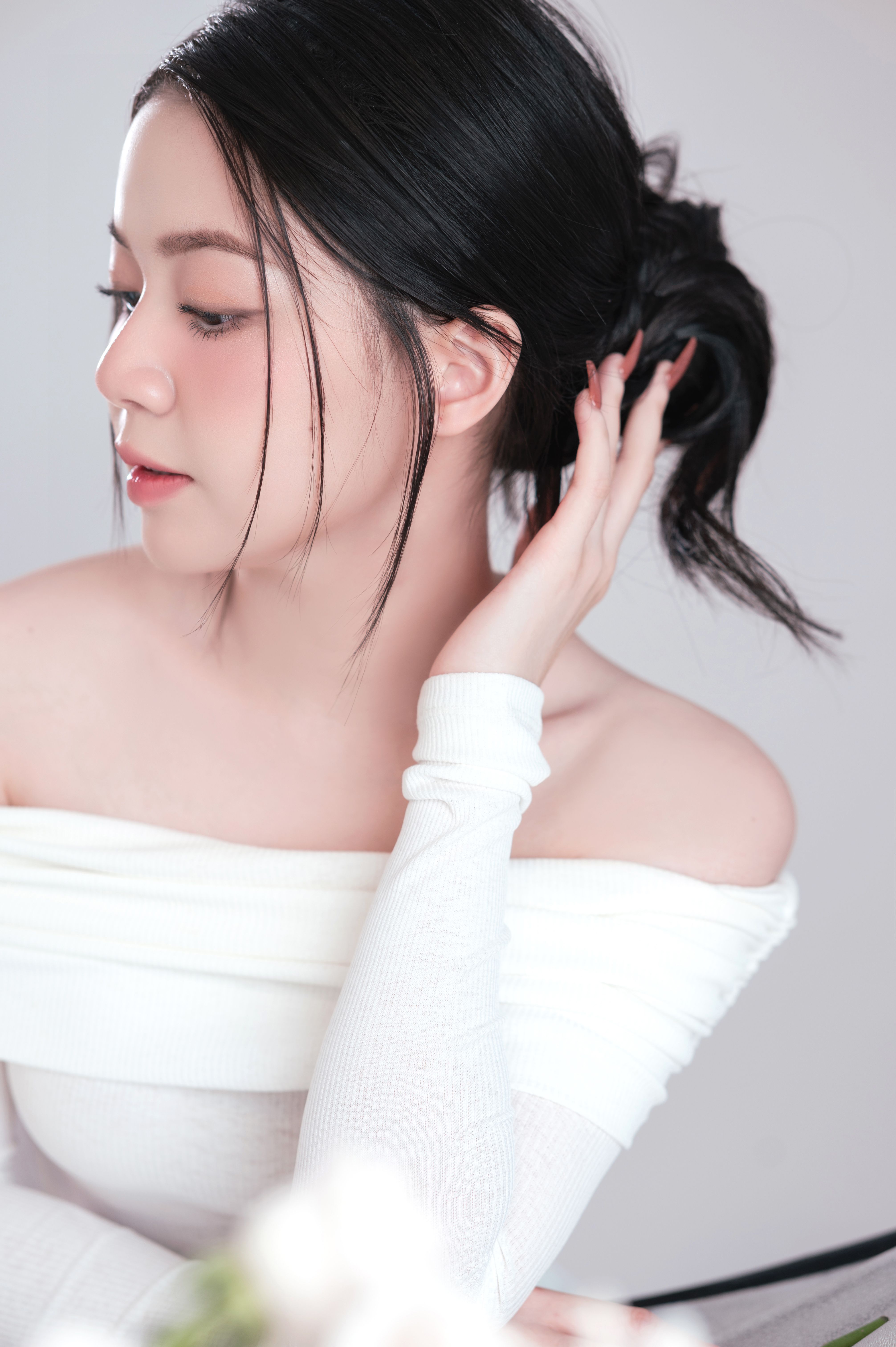 Studio portrait of an Asian woman with black hair adjusting her hairstyle, emphasizing elegance and fashion