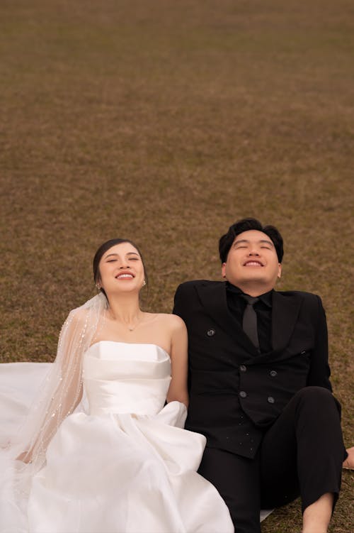 Smiling Newlyweds Sitting on Grassland with Eyes Closed