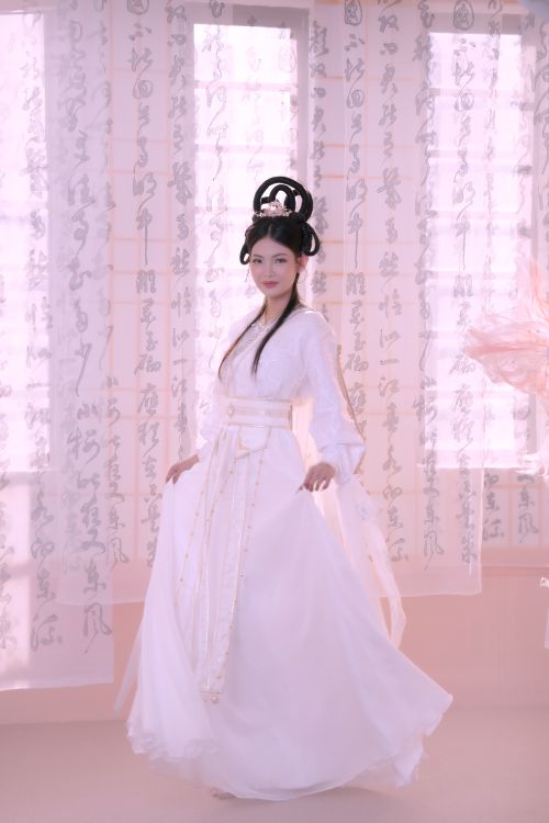 Free Asian woman in traditional white dress, standing elegantly by calligraphy curtains. Stock Photo