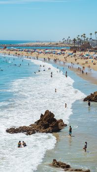 Crowded summer day at Newport Beach with people enjoying the surf and sunbathing.