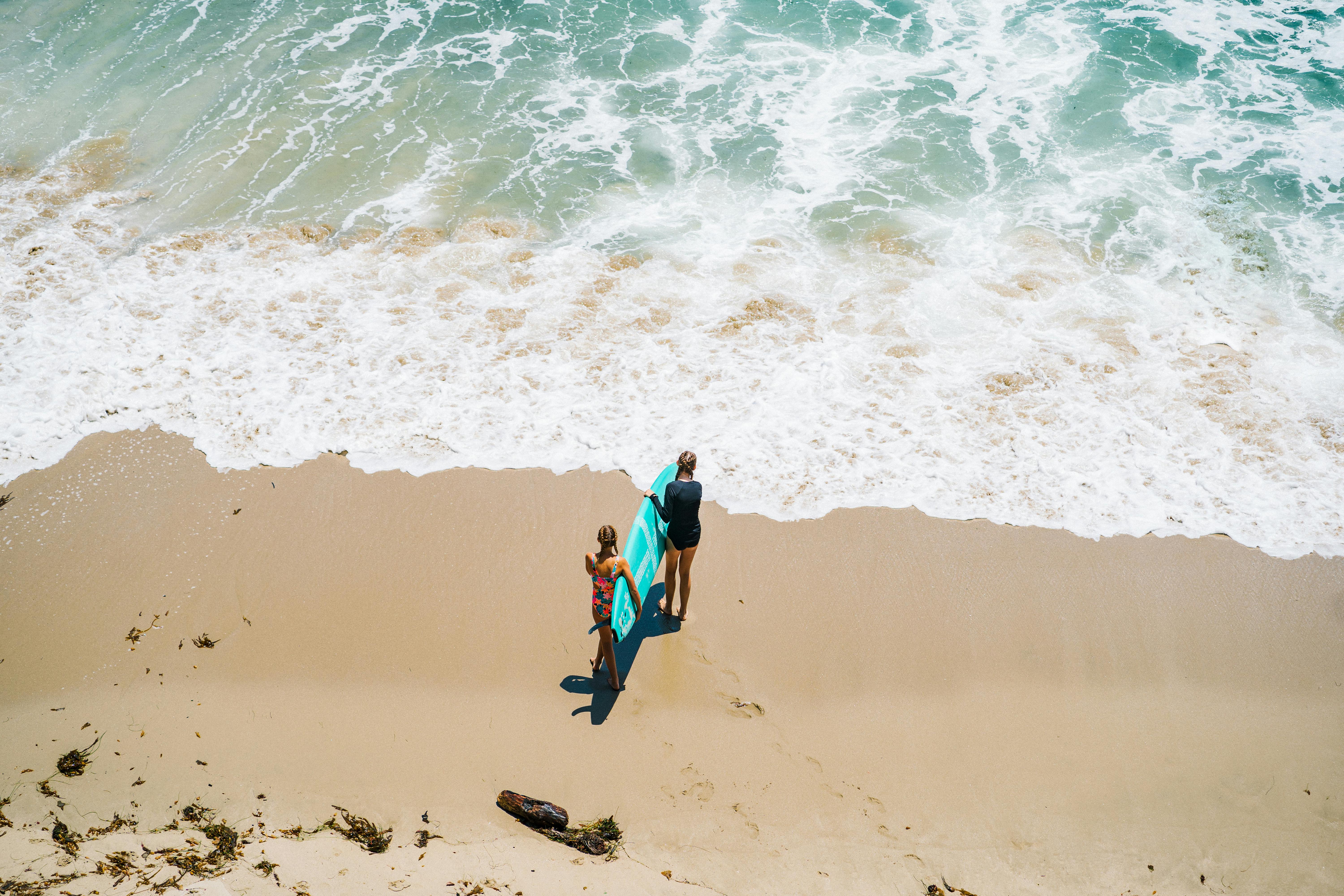 Aerial shot of surfers carrying their boards along a sunny beach shoreline.