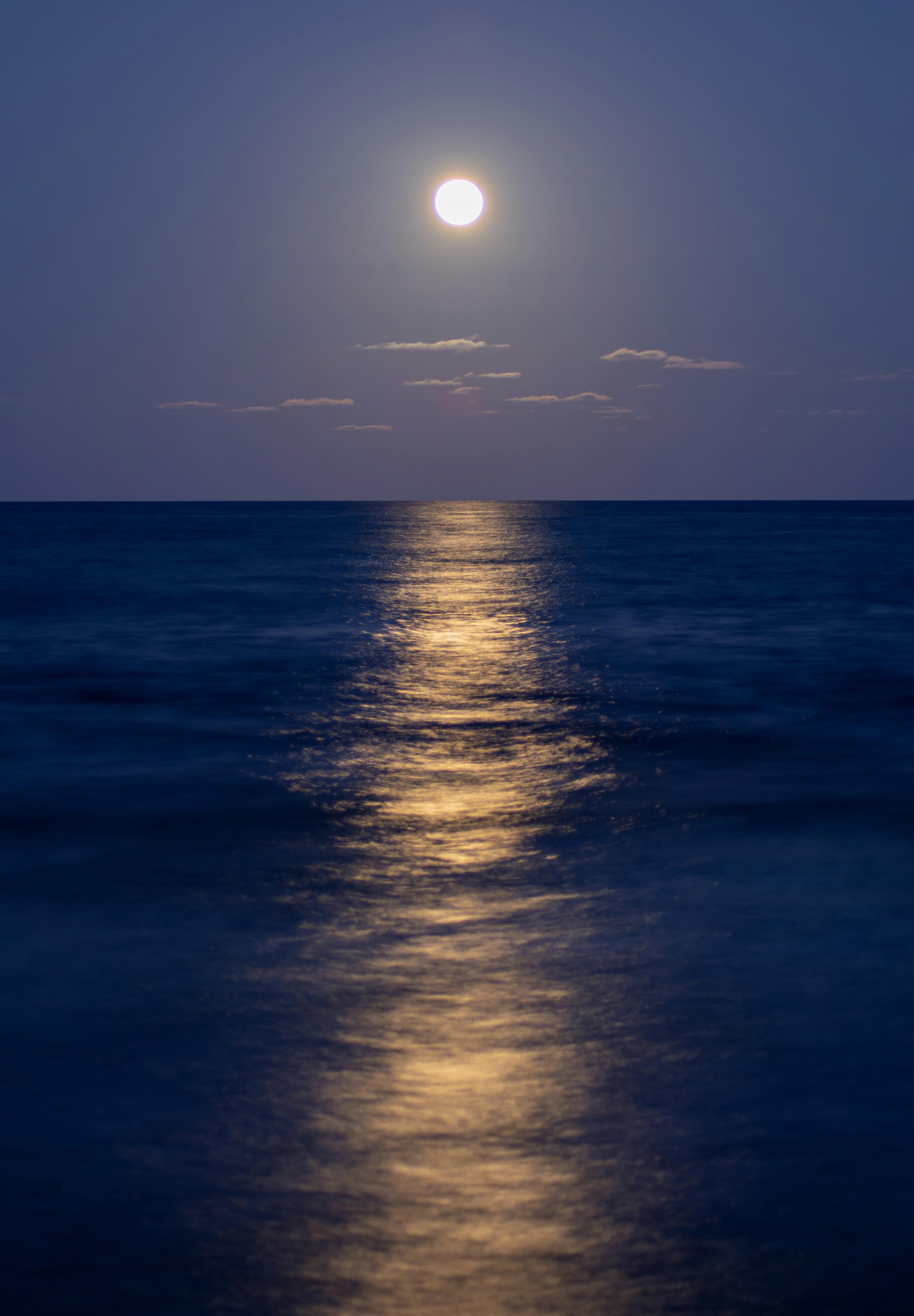 Stunning night view of the full moon reflecting over the calm Mediterranean Sea in Alicante, Spain.