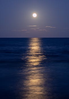 Stunning night view of the full moon reflecting over the calm Mediterranean Sea in Alicante, Spain.