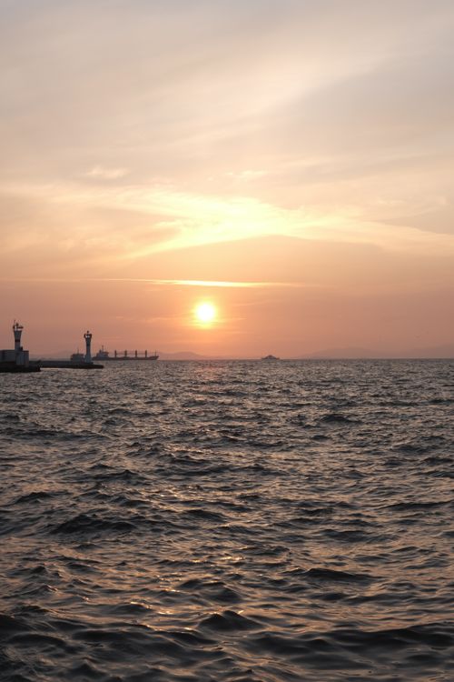 Free Beautiful sunrise over a calm harbor in İzmir, Türkiye, with gentle sea ripples and lighthouses. Stock Photo