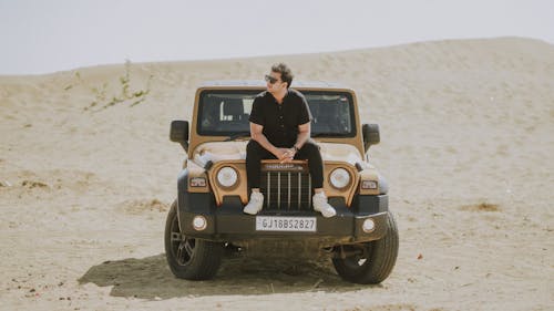 A man sitting on top of a jeep in the desert