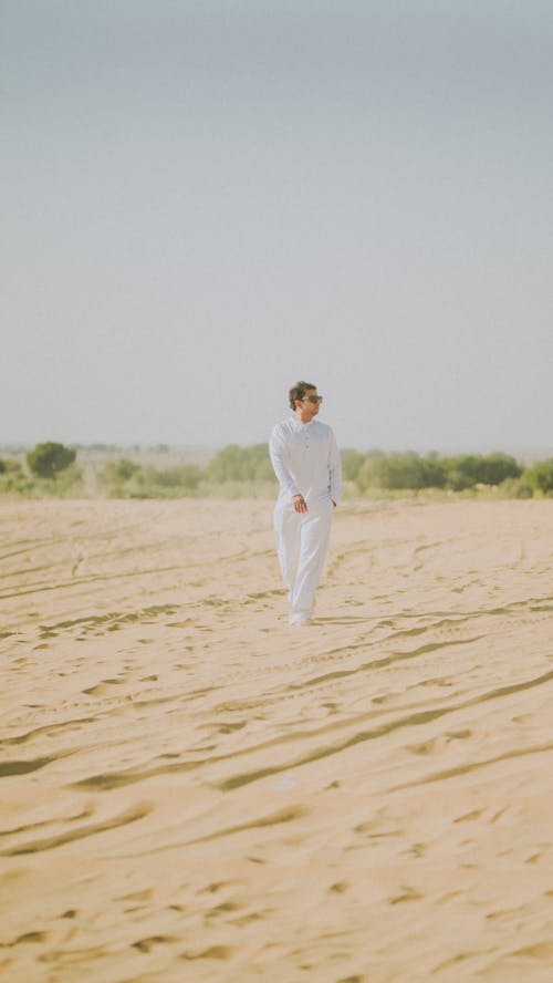 A man in white walking through the desert