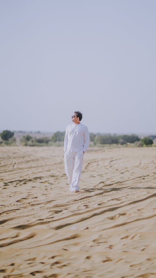 A man in white standing in the middle of a desert