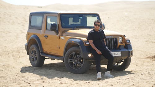 A man sitting in front of a jeep in the desert