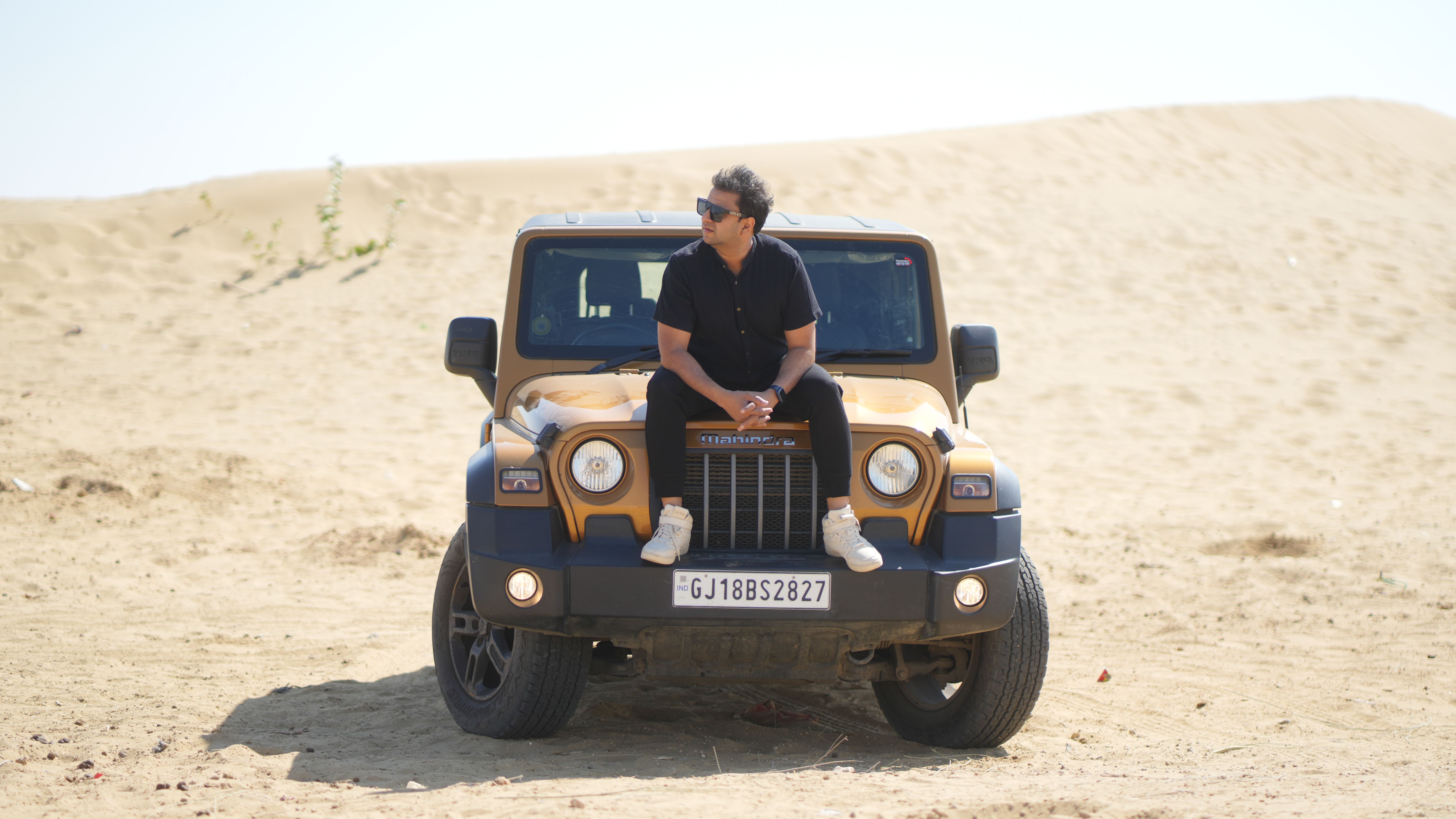A man sitting on a Jeep in the desert, showcasing adventure and freedom.