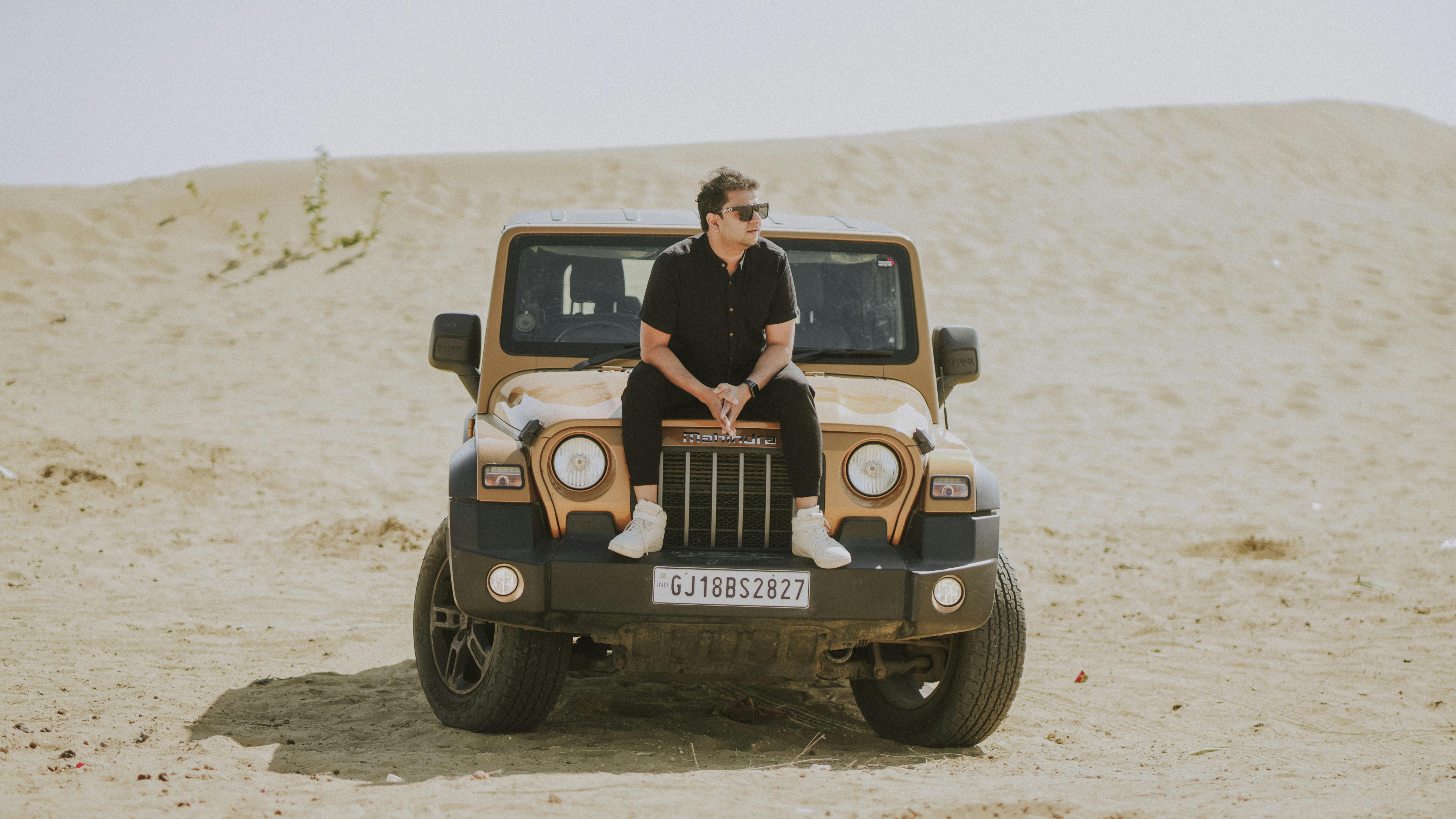 A man sitting on a parked SUV in a desert setting, showcasing modern off-road exploration.