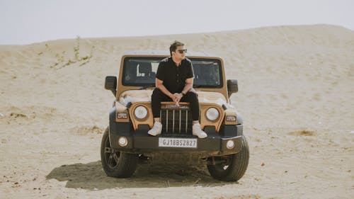 A man sitting on top of a jeep in the desert