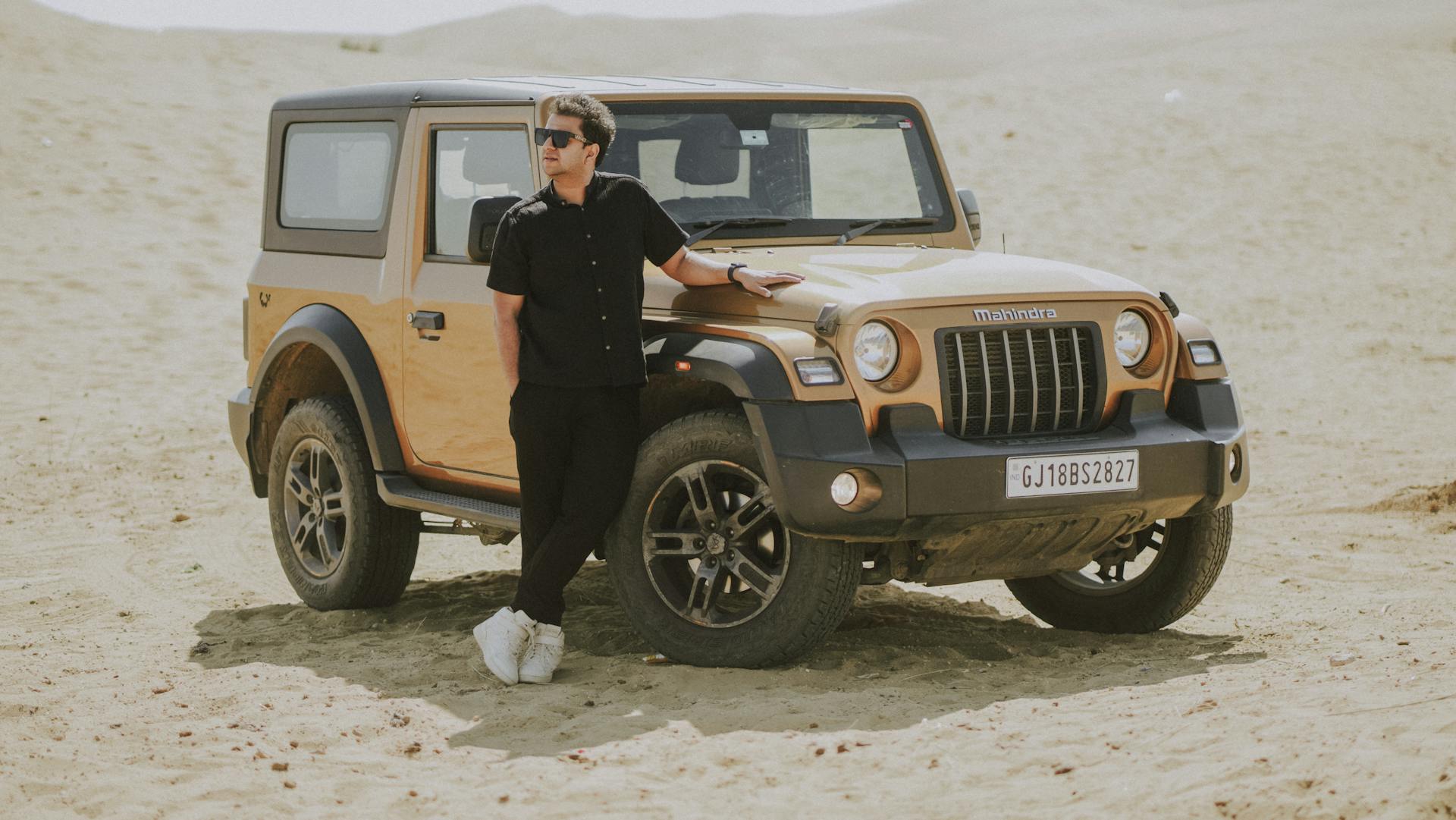 Man in Black Shirt Standing by Mahindra Thar on Sand