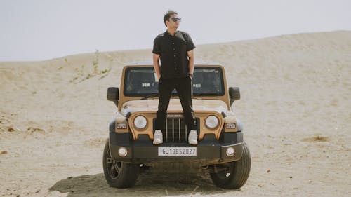 A man standing on top of a jeep in the desert