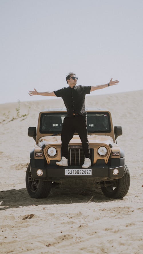 A man standing on top of a jeep in the desert