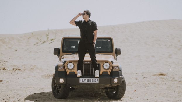 Man Standing on the Bumper of a Mahindra Thar SUV Parked in the Desert