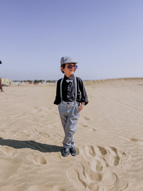 A little boy standing on the beach wearing sunglasses