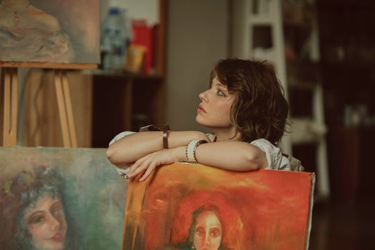 Woman artist reflecting in her studio surrounded by paintings, capturing creative inspiration.
