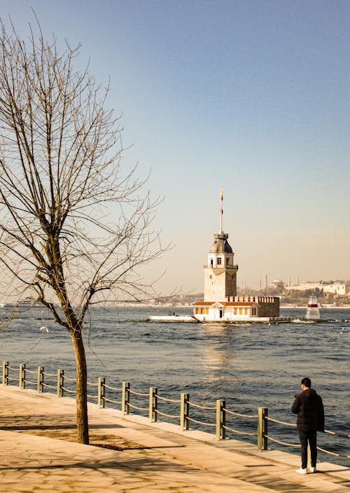 A man walking along the water near a lighthouse