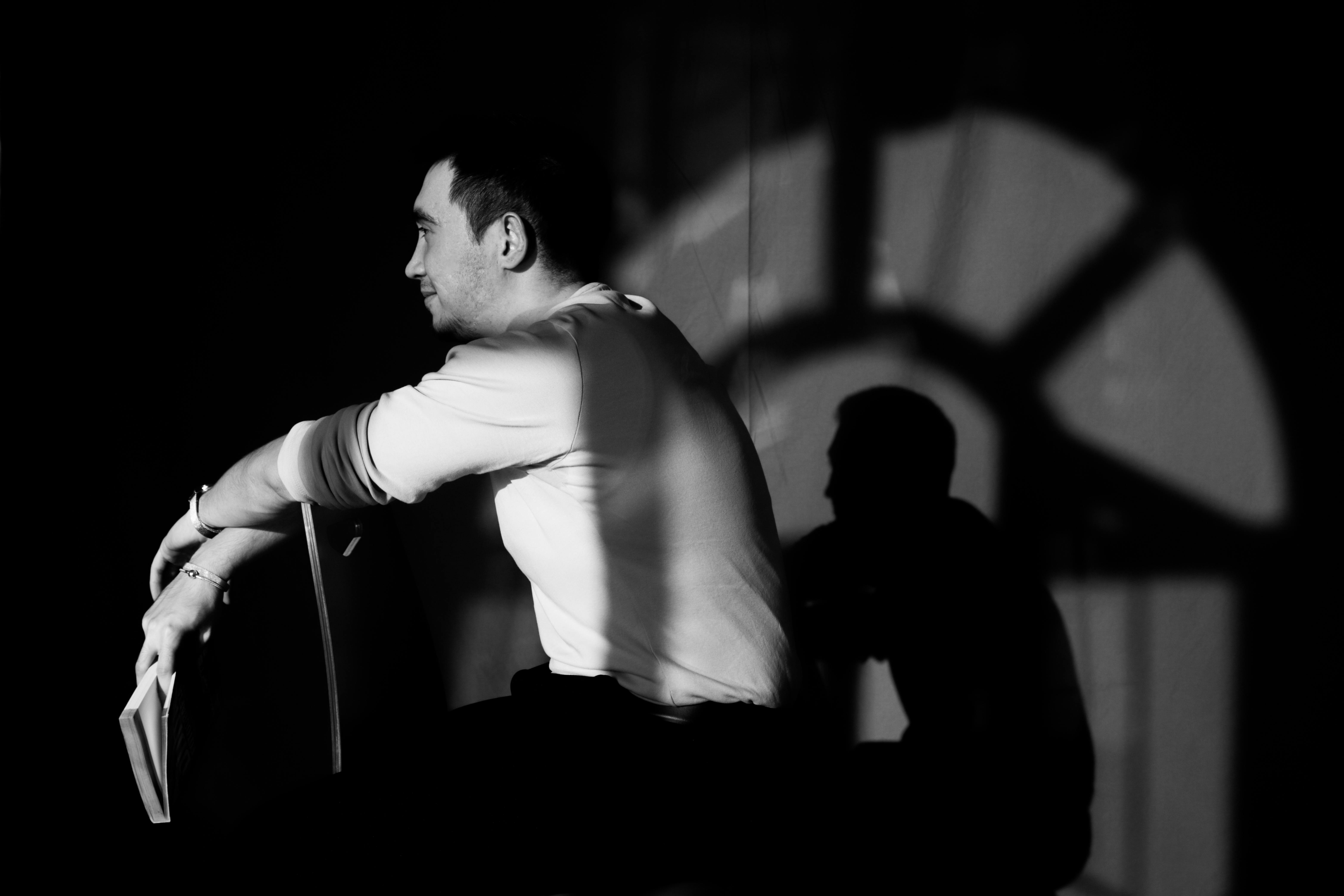 A man sitting on a chair, casting a dramatic shadow on the wall in black and white.