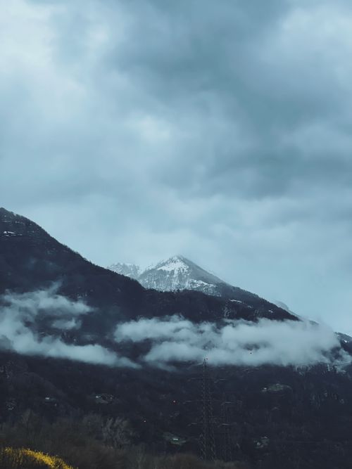 Free A scenic view of a snowcapped mountain peak surrounded by clouds with a moody atmosphere. Stock Photo