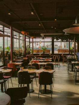 A spacious and cozy restaurant interior with modern design featuring tables, chairs, and ambient lighting.