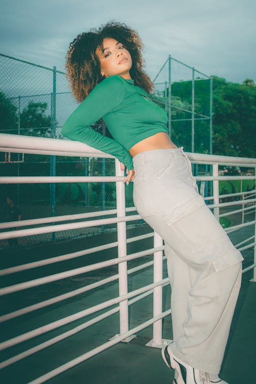 A woman in green top and white pants standing on a railing