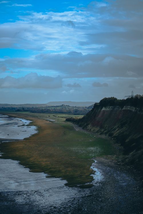 Free A scenic aerial view of a rugged coastline with cliffs and sea under a vivid blue sky. Stock Photo