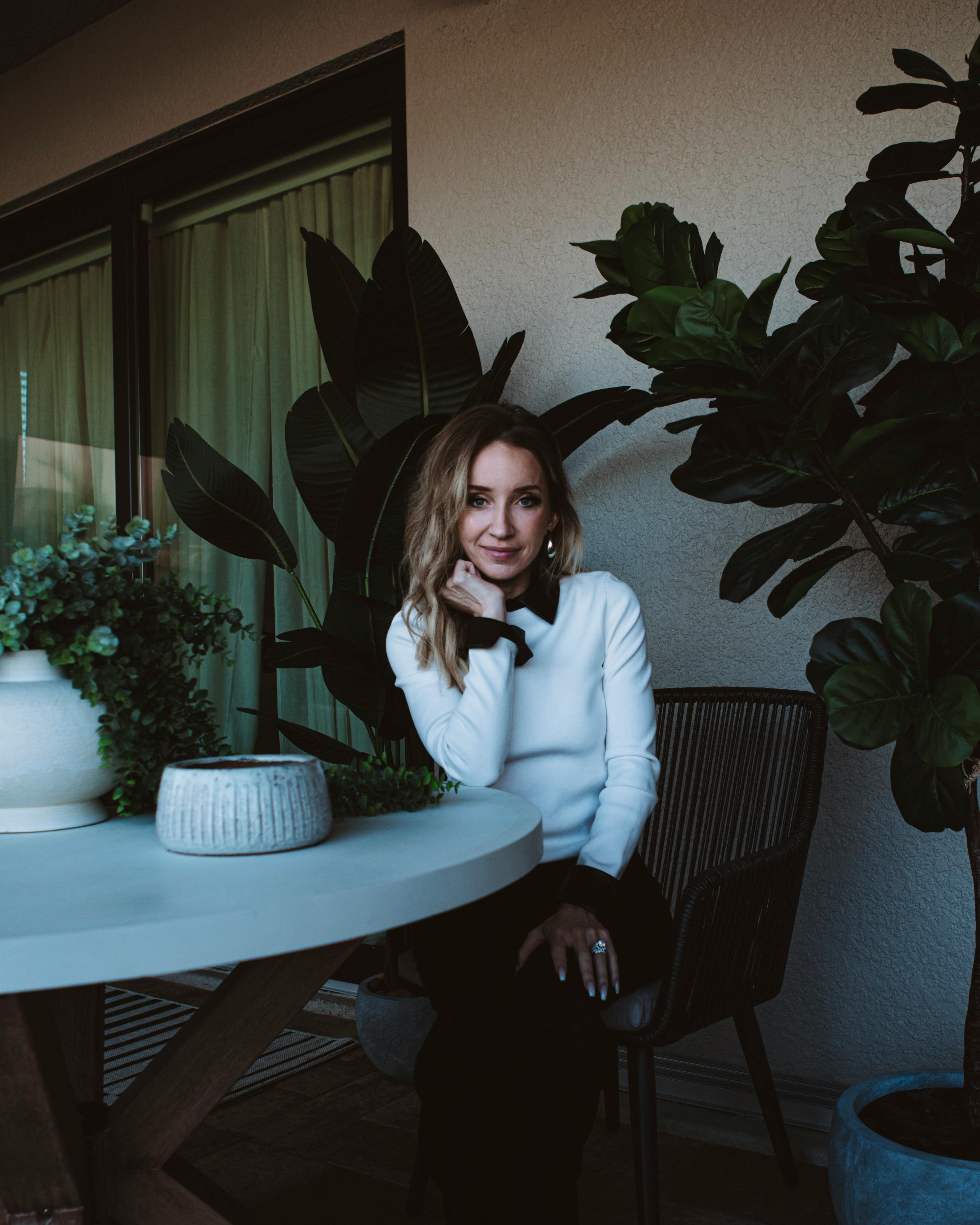 Elegant adult woman in a white sweater sitting among houseplants, creating a serene indoor atmosphere.