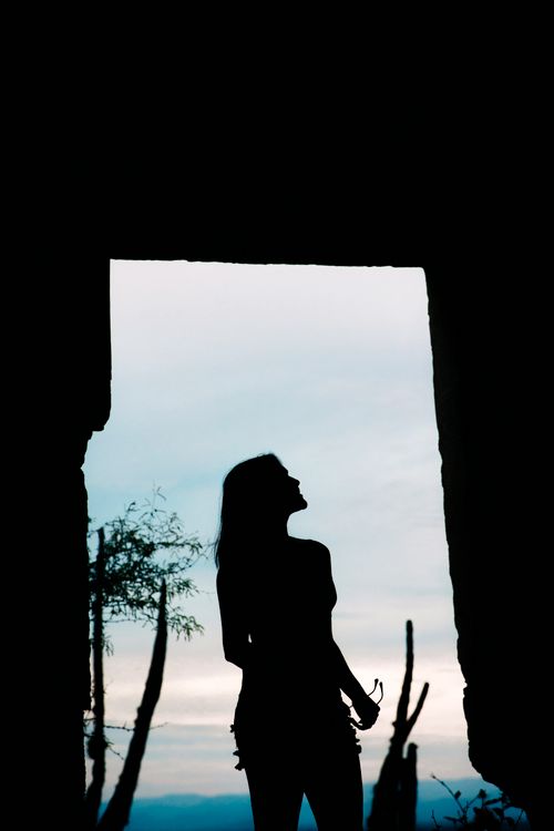 Free A striking silhouette of a woman gazing upwards in a doorway at twilight, capturing a serene moment. Stock Photo