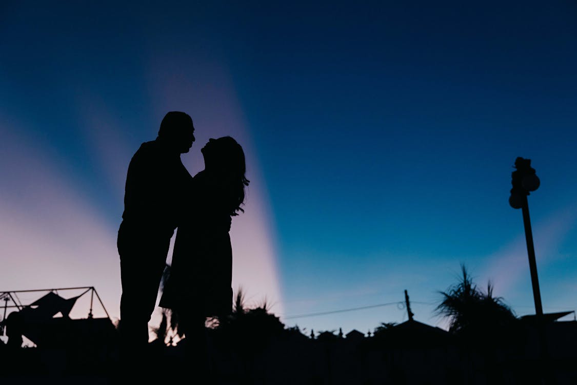 A silhouette of a couple standing in front of a blue sky