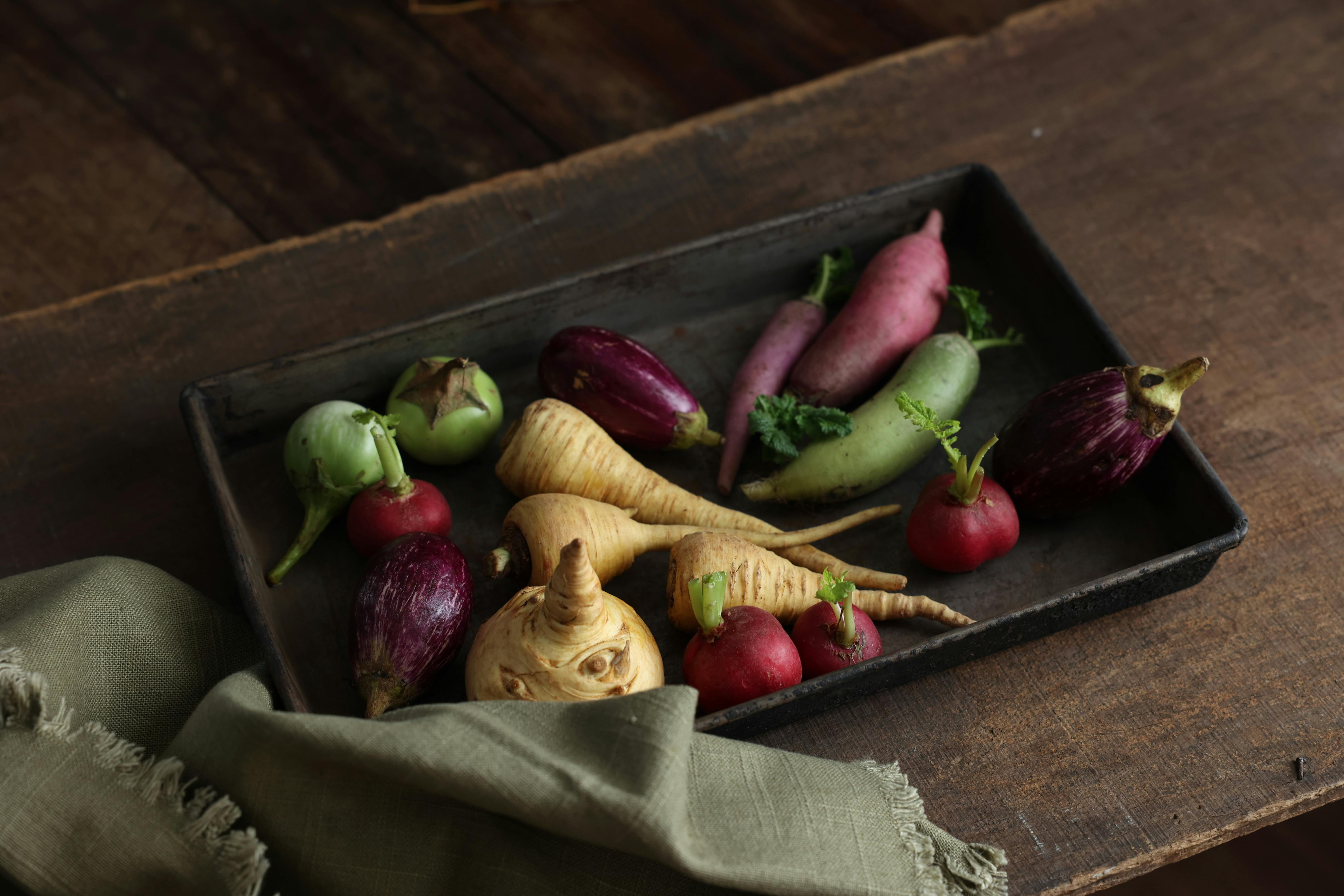 Free A rustic tray featuring a variety of fresh vegetables, including radishes and parsnips, on a wooden surface. Stock Photo