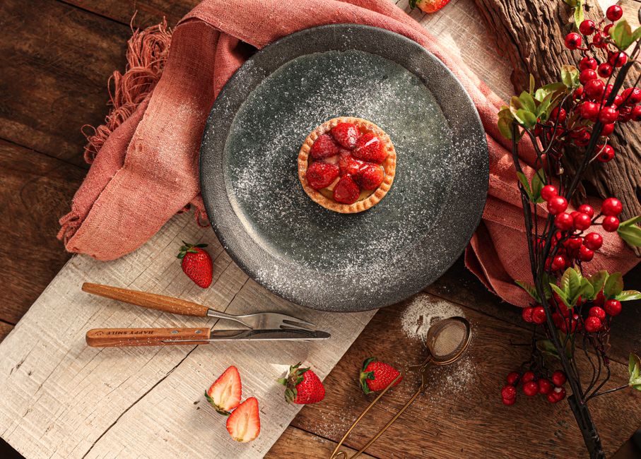 A delicious strawberry tart dusted with powdered sugar on a rustic wooden table.