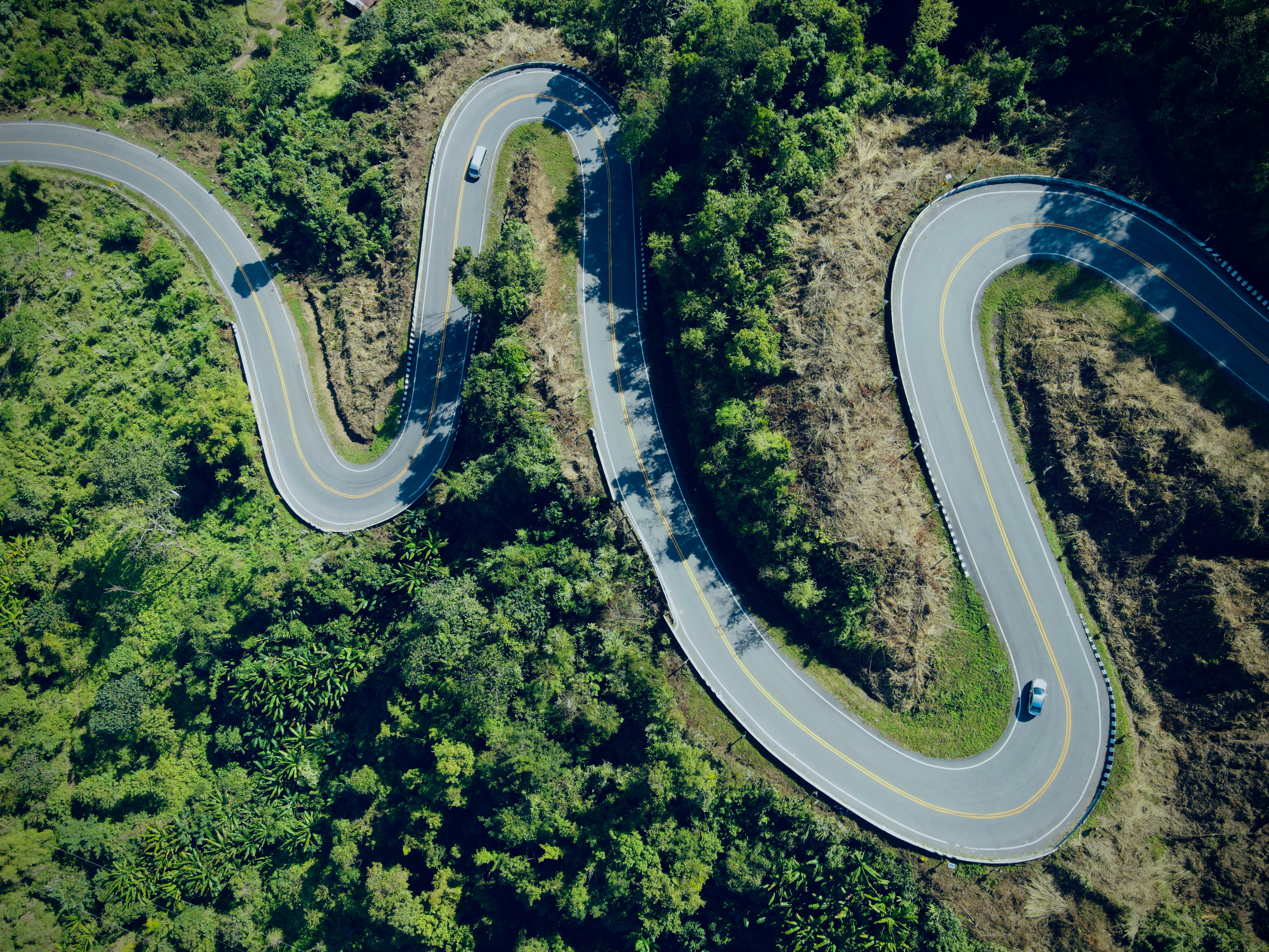 Aerial view of a winding road through lush forest in Thailand, capturing nature's beauty.