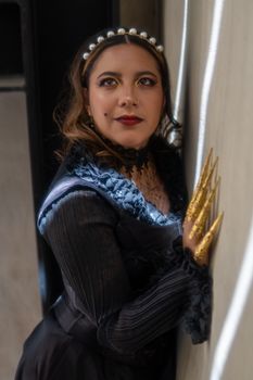 Woman in vintage black dress with gold finger claws poses against wall in Mexico City.