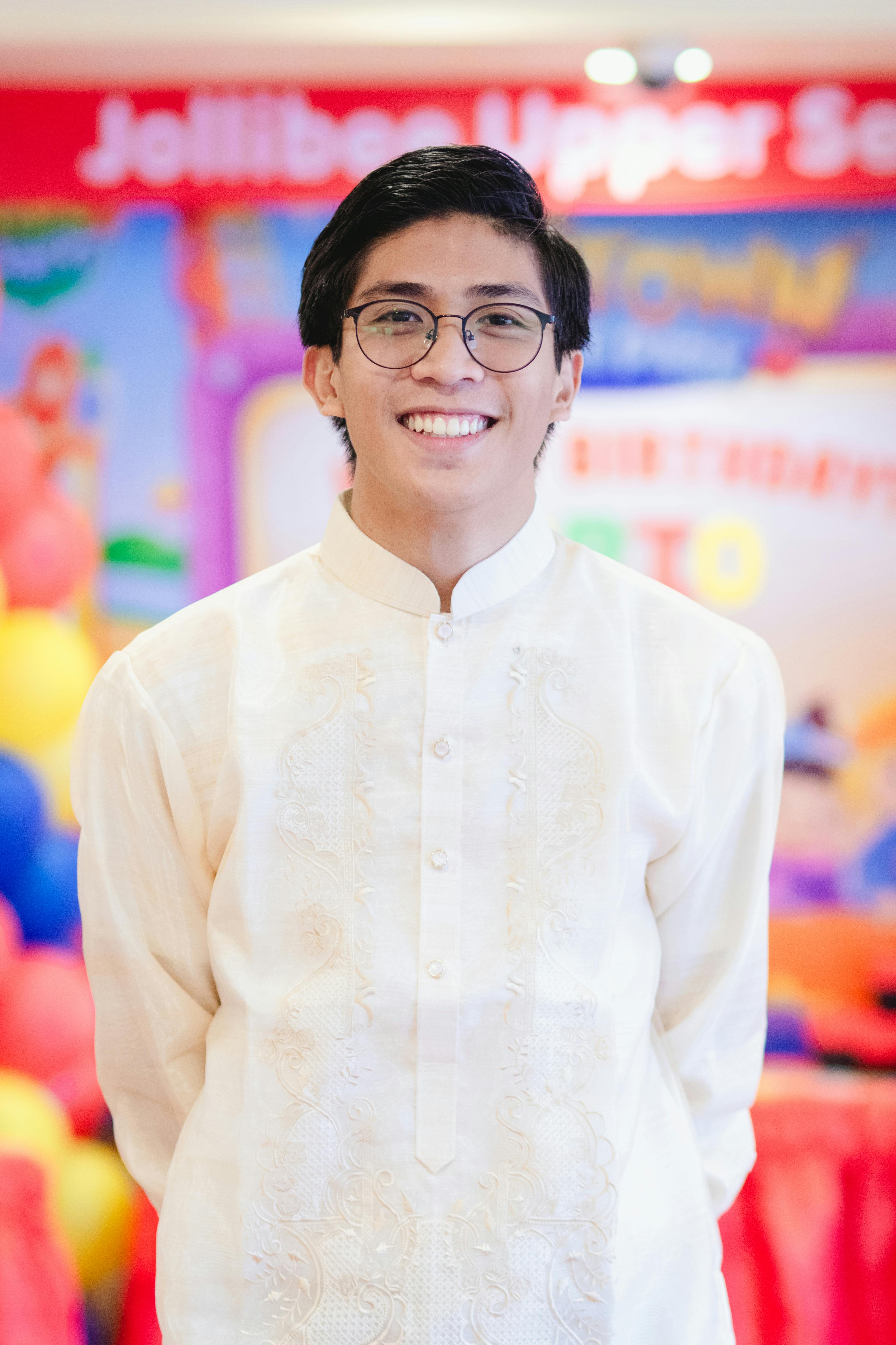 Young man in traditional Filipino attire smiling at a colorful indoor event setting.