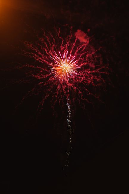 A bright red firework explodes against the dark night sky, showcasing sparkling trails and a radiant burst.