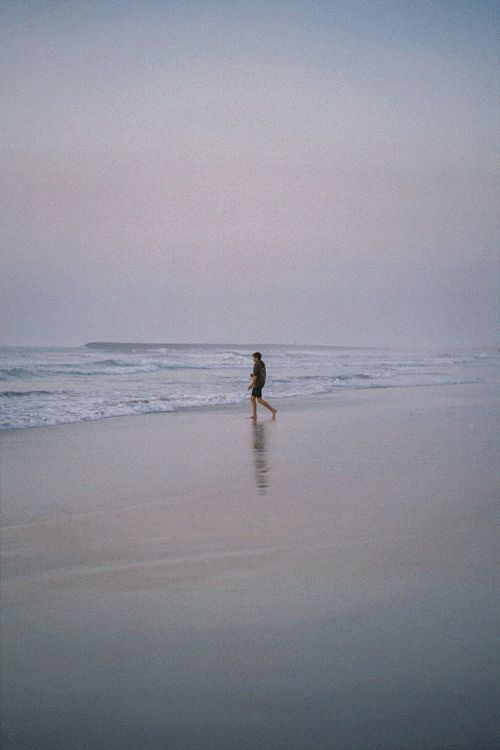 Free A lone individual walks by the ocean at dawn, reflecting tranquility and nature's beauty. Stock Photo