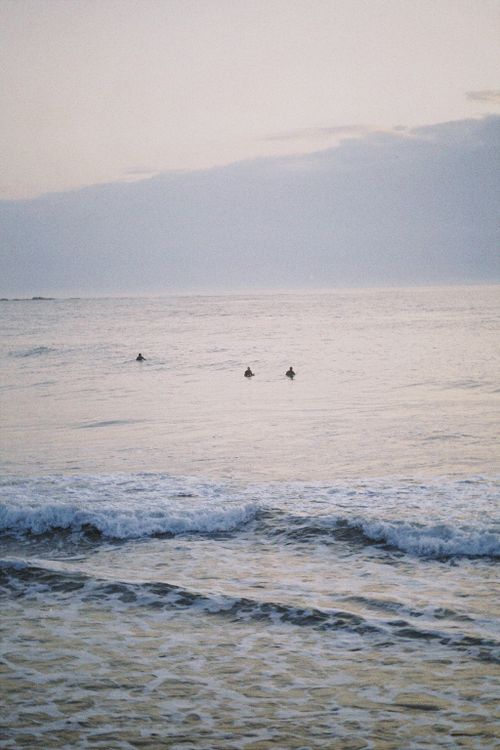 Free Three surfers awaiting waves at dawn in a calm ocean setting, capturing tranquility and anticipation. Stock Photo