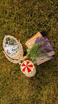 Aesthetic outdoor arrangement of vintage mirror, book, and lavender flowers on grass.