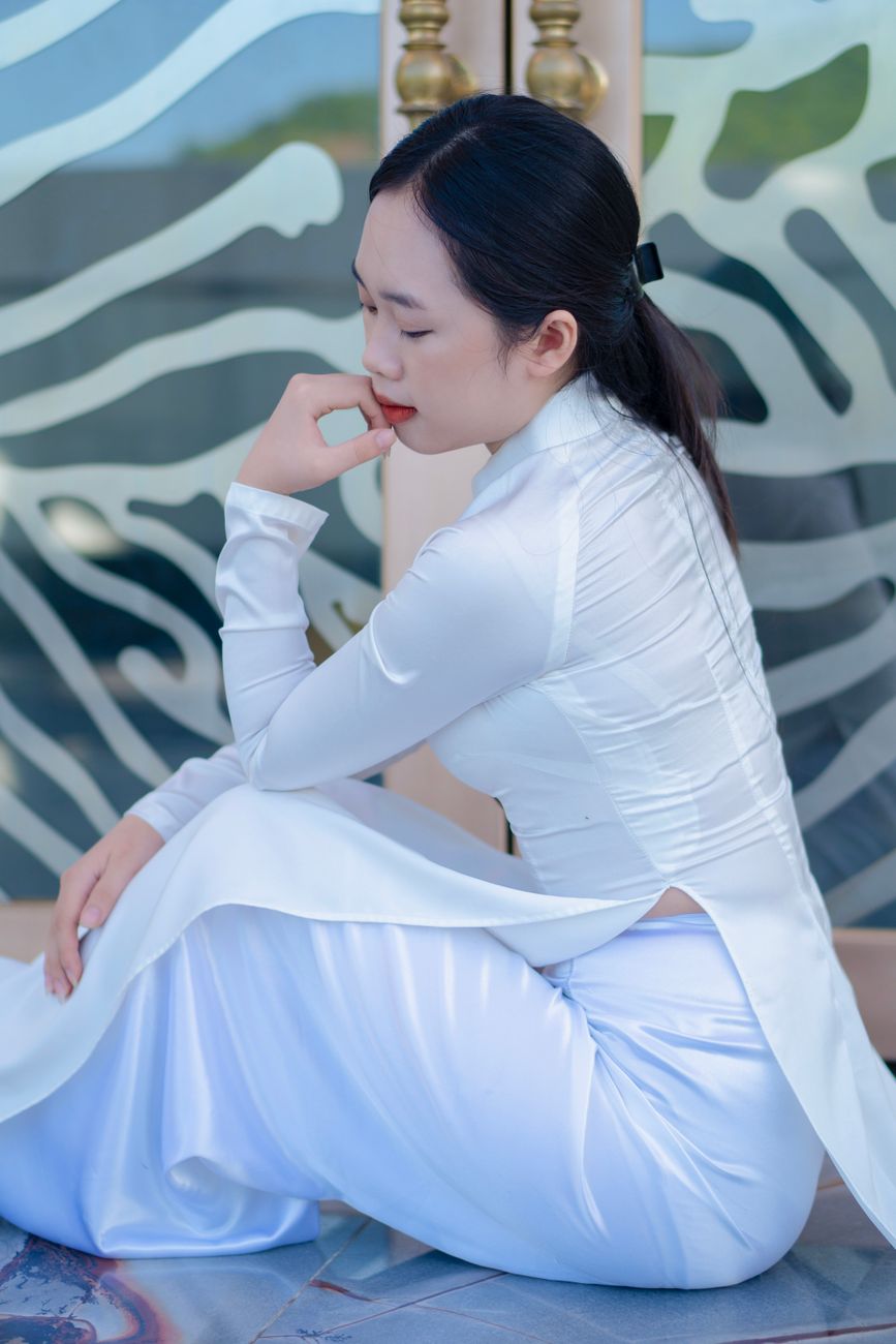 Portrait of a woman in a white Ao Dai seated indoors. Perfect for fashion and culture themes.