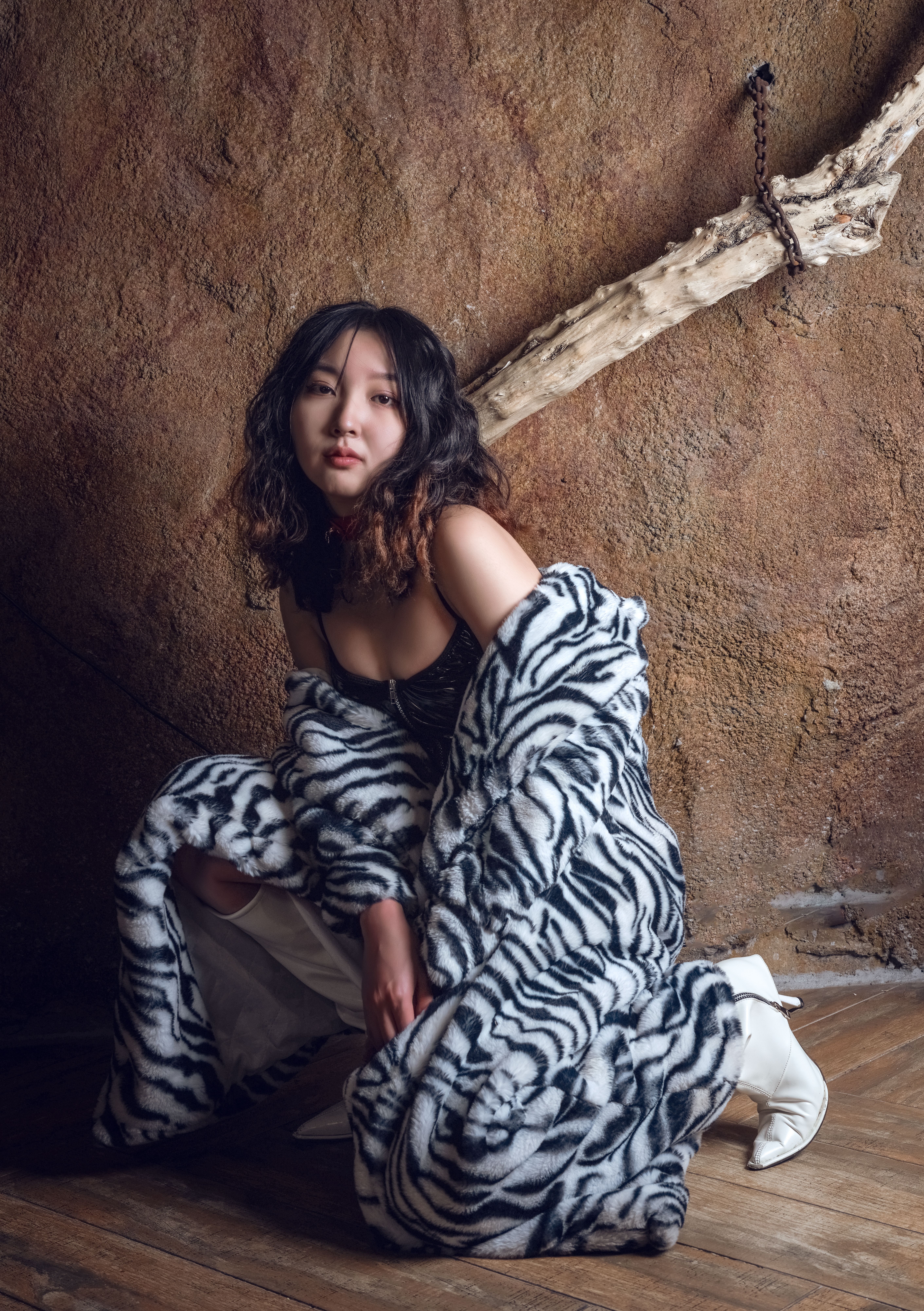 Young woman poses in a zebra print faux fur coat against a rustic wall.