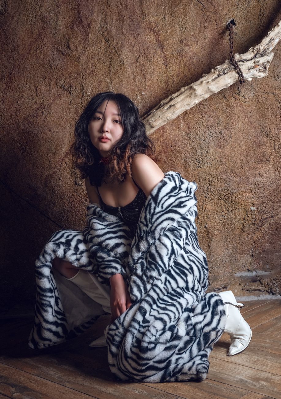 Young woman poses in a zebra print faux fur coat against a rustic wall.
