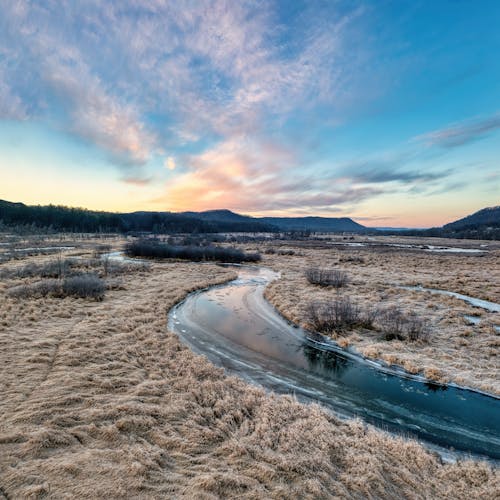 View of a Dry Grass Field, Frozen River and Hills in the Distance 